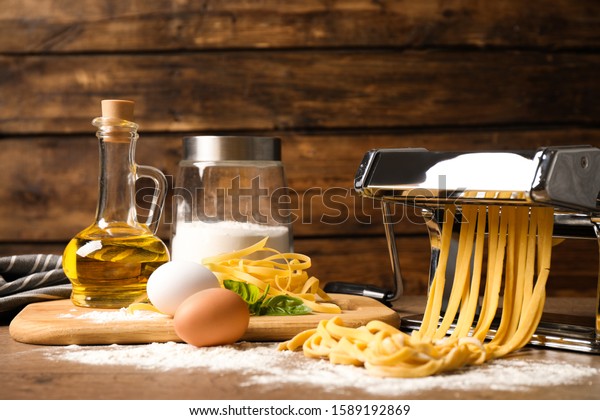 Pasta maker machine with dough and products on\
wooden table