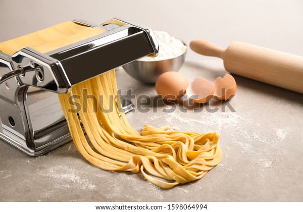Pasta\
maker machine with dough and products on grey\
table