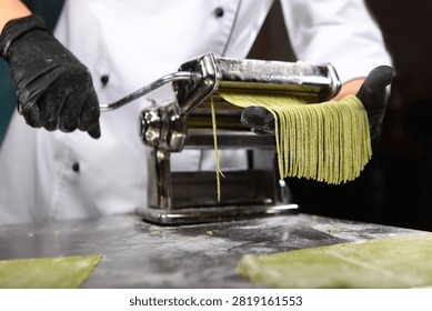 Pasta making machine and dough rolling. Chef makes dough with spinach. Homemade pasta. Making pasta with spinach. Paste is green