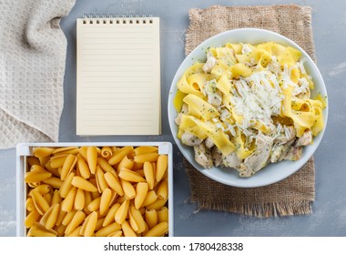 Pasta meal with copybook, raw pasta, kitchen towel in a plate on plaster and piece of sack background, top view.  - Powered by Shutterstock