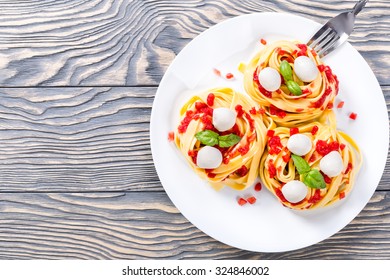 Pasta With Mozzarella, Tomatoes Decorated With Basil Leaves On The White Dish With Fork On The Wooden Background, Close-up, Top View 