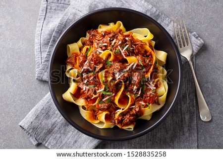 Pasta pappardelle with beef ragout sauce in black bowl. Grey background. Top view.
