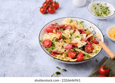 Pasta salad with farfalle pasta, cherry tomatoes, smoked duck meat and microgreens in a white plate on a light concrete background. Italian Cuisine. Pasta salad recipes.