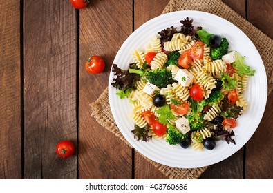 Pasta salad with tomato, broccoli, black olives,  and cheese feta. Top view