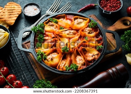 Pasta. pasta shells baked with meat, tomatoes and parmesan. In a frying pan. On a black stone background.