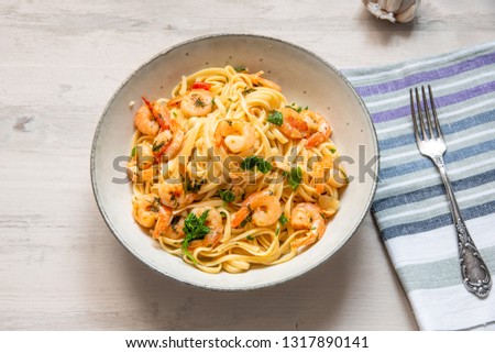 Pasta with shrimps, parsley and chilli peppers on a plate, on a light wooden background - traditional Mediterranean linguine with seafood, Italian cuisine.