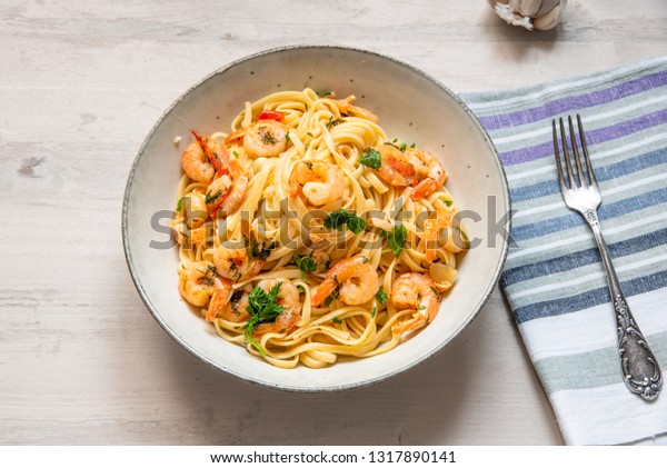 Pasta with shrimps, parsley and\
chilli peppers on a plate, on a light wooden background -\
traditional Mediterranean linguine with seafood, Italian\
cuisine.