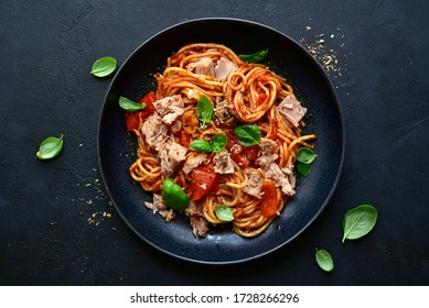 Pasta spaggeti with tuna and tomato sauce in a black bowl on a dark slate, stone or concrete background. Top view with copy space.