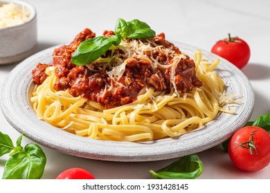 Pasta spaghetti bolognese with minced beef sauce, tomatoes, parmesan cheese and fresh basil in a plate on white table. Italian food - Shutterstock ID 1931428145