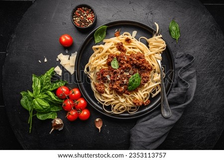 Pasta spaghetti bolognese with minced beef sauce, tomatoes, parmesan cheese and fresh basil in a plate on black tile background. Italian food, top view