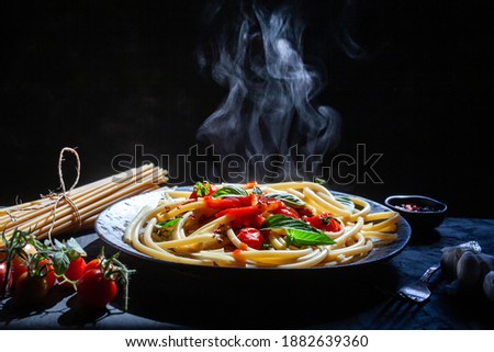 Pasta, spaghetti with tomato sauce in black bowl. Grey stone background.,  on dark Background with smoke and steam, view. Selective Focus at the front.hot food concept