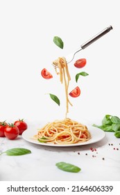 pasta with tomatoes and basil on a white background. Fork with pasta flying on a white background with tomatoes - Shutterstock ID 2164606339