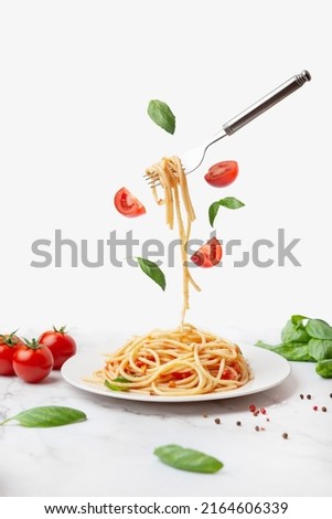 pasta with tomatoes and basil on a white background. Fork with pasta flying on a white background with tomatoes