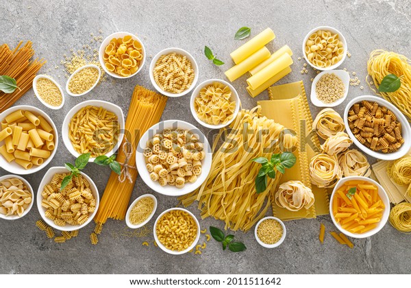 Pasta.\
Various kinds of uncooked pasta and noodles over stone background,\
top view with copy space for text. Italian food culinary concept.\
Collection of different raw pasta on cooking\
table