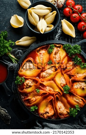 Paste. Large pasta shells baked with meat in tomato sauce. In a frying pan. On a black stone background.