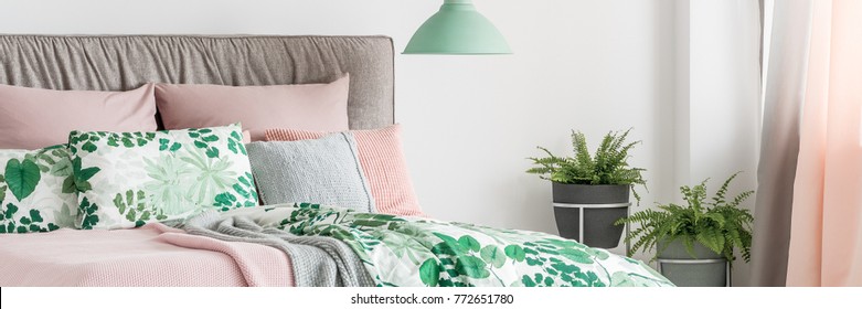 Pastel bed with headboard, decorative cushions and botanic patterned bedding next to window