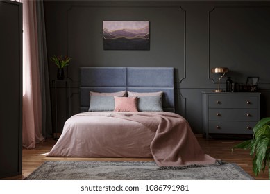 Pastel blanket on bed in pink and blue bedroom interior with gold lamp on grey cabinet