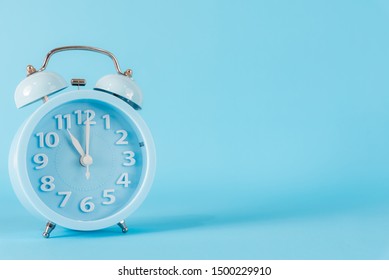 Pastel blue alarm clock with eleven o’clock on blue background. 11 am, 11 pm. Time concept.