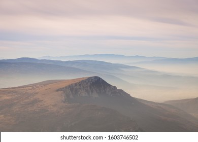 Pastel Color Palette Of Misty Landscape With Rocky Mountain Peak Rising Above Fog Covered Valleys And Mountain Layers During Colorful Sunrise