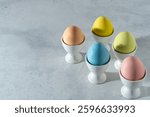 pastel colored easter egg assortment in white cups in diagonal direction on the right on a white marble background. high angle view, Copy space.