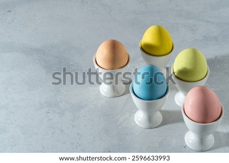 pastel colored easter egg assortment in white cups in diagonal direction on the right on a white marble background. high angle view, Copy space.