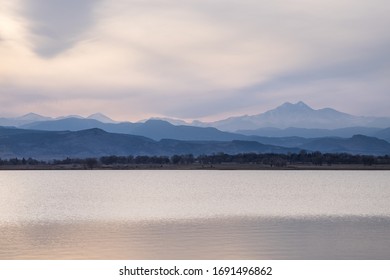 Pastel colored hazy Rocky Mountains landscape with lake in foreground 