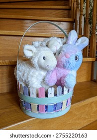 A pastel Easter basket filled with a fluffy plush bunny and two soft lamb stuffed animals, arranged on wooden stairs for seasonal decor, gift inspiration, or playful children’s room styling.