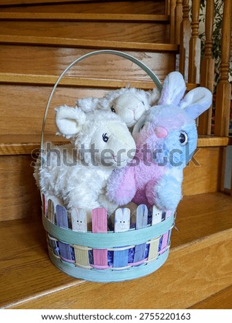 A pastel Easter basket filled with a fluffy plush bunny and two soft lamb stuffed animals, arranged on wooden stairs for seasonal decor, gift inspiration, or playful children’s room styling.