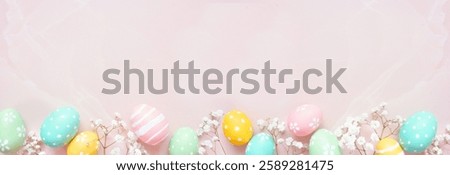 Pastel Easter eggs and white spring flowers. Top view bottom border against a soft pink stone banner background. Copy space.