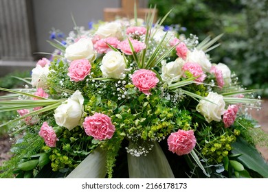 Pastel Funeral Flowers On A Grave In Front Of A Wooden Cross In Blurred Background