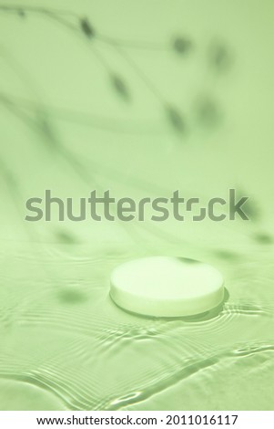 Pastel green colored abstract nature scene with white cylinder podium on transparent water with waves and soft plants shadow. Pedestal for cosmetic product and packaging mockups display presentation