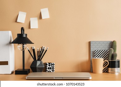 Pastel orange creative desk with laptop, plant, office accessories, cacti and sticky notes. Creative workspace.