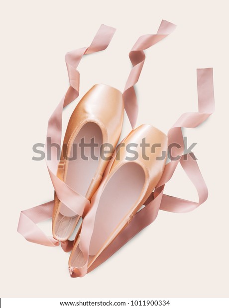 Pastel pink ballet shoes\
background. New pointe shoes with satin ribbon lay on white\
isolated backdrop