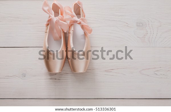 Pastel pink ballet shoes background. New pointe\
shoes with satin ribbon lay on white rustic shubby chic wood, top\
view with copy space