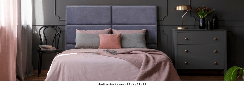 Pastel Pink Bedclothes On King-size Bed With Soft Bedhead Standing In Dark Bedroom Interior With Gold Lamp And Fresh Tulips On Grey Cupboard