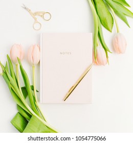 Pastel pink tulip flowers, notebook, golden scissors and pen. Flat lay, top view blogger composition.