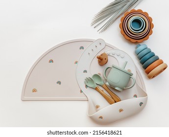 Pastel silicone collection of tableware, bibs, accessories, Montessori toys for children on blue background. Baby accessories, tableware concept.