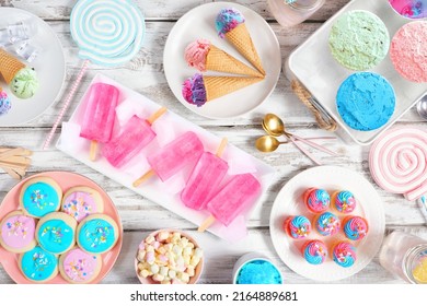 Pastel summer sweets table scene. Assortment of ice cream, popsicles, cookies and treats. Above view over a rustic white wood background.