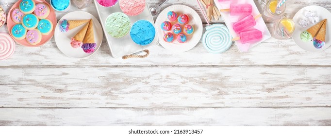 Pastel summer sweets top border. Assortment of ice cream, popsicles, cookies and treats. Overhead view over a rustic white wood banner background. Copy space.