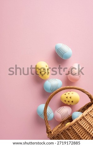 Pastel vertical Easter eggs with stripes and spots spill from a wicker basket onto a pink backdrop, conveying festive spring celebration and warm greeting for Easter occasions