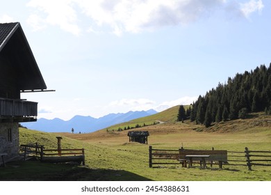 pastoral mountain landscape with wooden dwellings and fences in the meadow and a hazy blue mountain range in the distance - Powered by Shutterstock