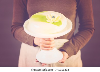 Pastre chef holding gourmet mousse cake on a white cake stand.