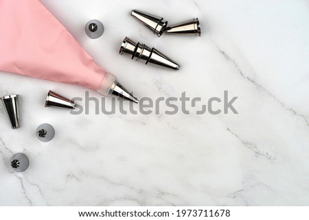 Pastry bag cream pink injector for cake dessert decoration, supplies kit icing piping, stainless steel nozzle tips. DIY tools on white marble background. Cooking bakery concept with copy space