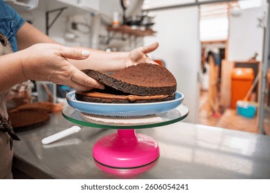 Pastry chef assembling a two layer chocolate cake, placing a layer on a rotating cake stand in a professional kitchen