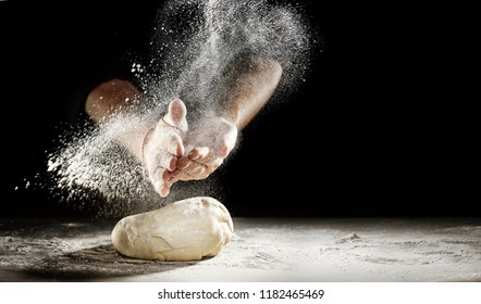 Pastry chef clapping his hands to dust a mound of freshly prepared pastry with flour in a freeze motion of a cloud of flour midair on black with copy space - Powered by Shutterstock