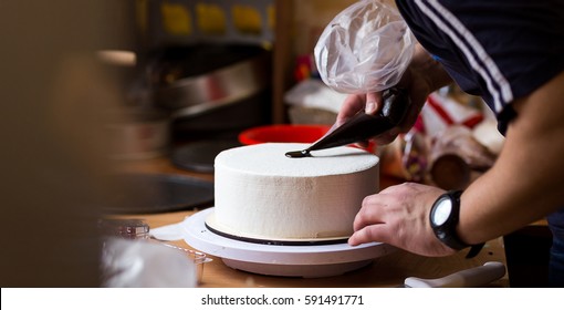 Pastry Chef Confectioner In The Kitchen Decorating A Cake Of Chocolate,fruit,candies