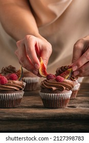 Pastry chef decorates muffin with raspberries and figs. Close up photo of cupcakes preparation. Vertical frame.
