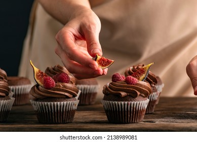 Pastry chef decorates muffins with raspberries and figs. Close up of cupcakes preparation
