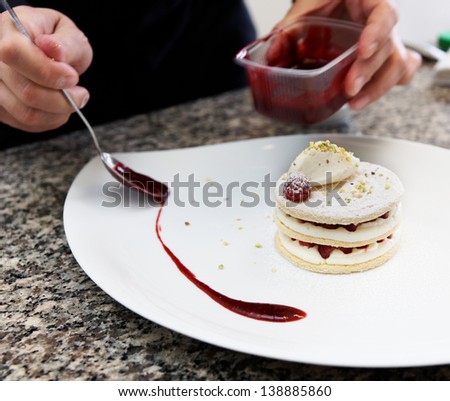 Pastry chef is decorating the dessert with red berry sauce