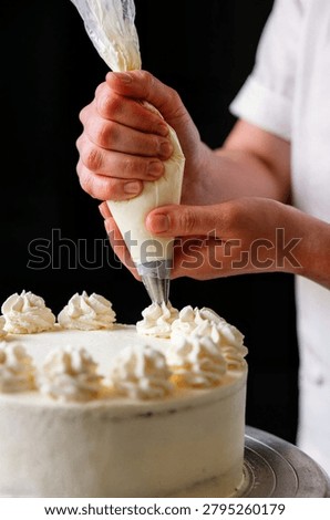 Pastry chef hands squeezing white cream from piping bag onto cake for professional bakery advertisement and culinary course